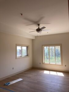 Bright bedroom with wood-look flooring, ceiling fan, and large windows overlooking trees in a Prices Fork Village Apartments unit